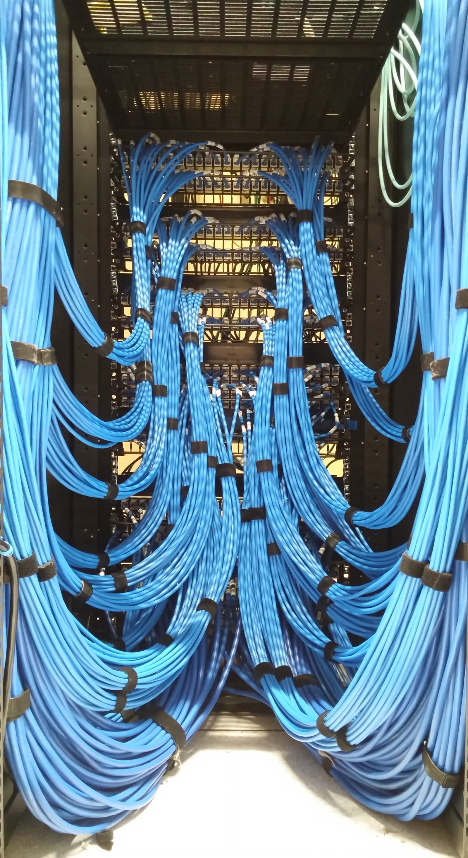 Parte de trás de um patch panel de datacenter, com cabos azuis amarrados em feixes